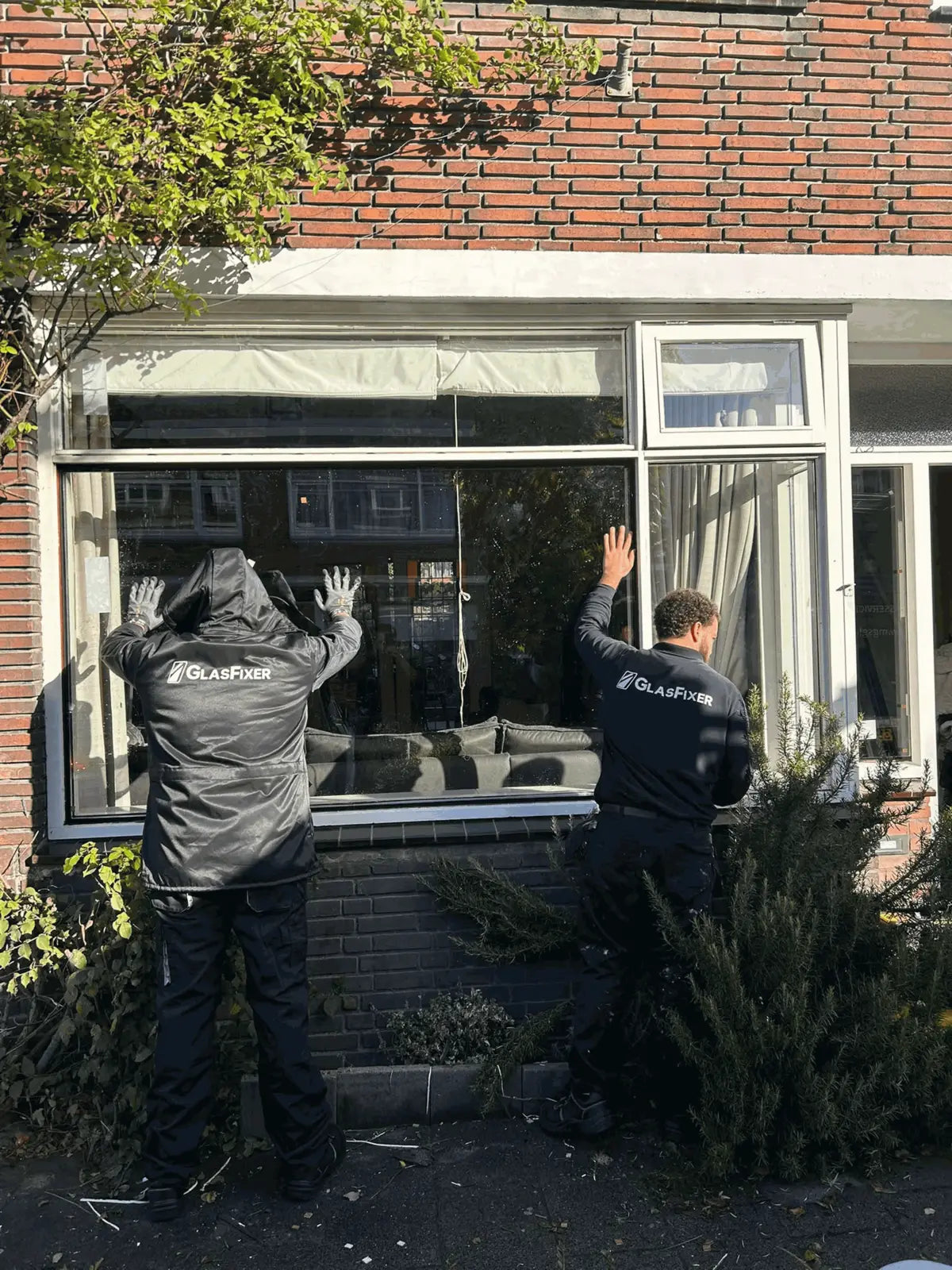 Twee monteurs van Glasfixer plaatsen een nieuwe ruit in een bakstenen rijtjeshuis